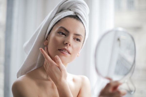 Woman with her hair wrapped in a towel checking her skin in a hand mirror