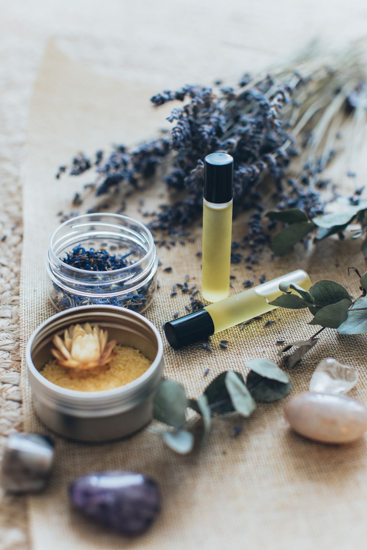 Aromatherapy oils in roller bottles beside dried lavender, eucalyptus and crystals