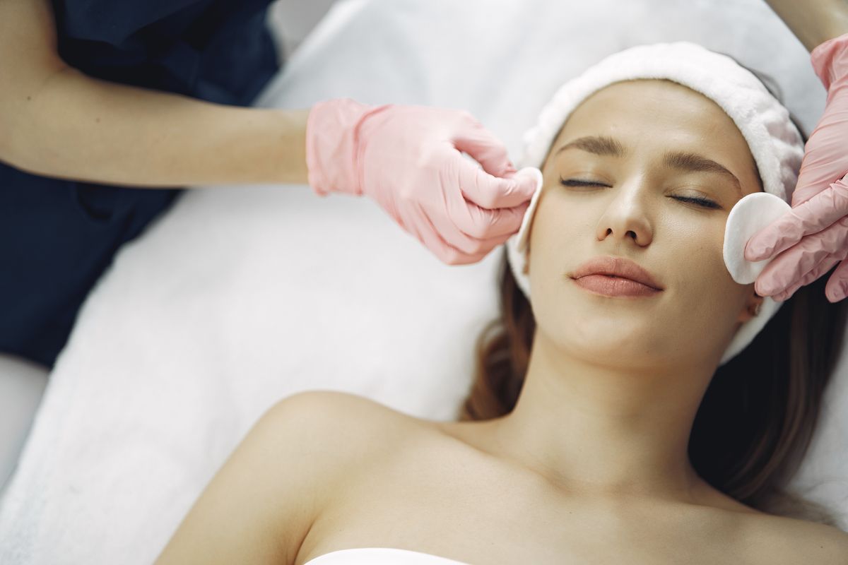 Therapist in pink gloves cleansing a client's face with cotton pads