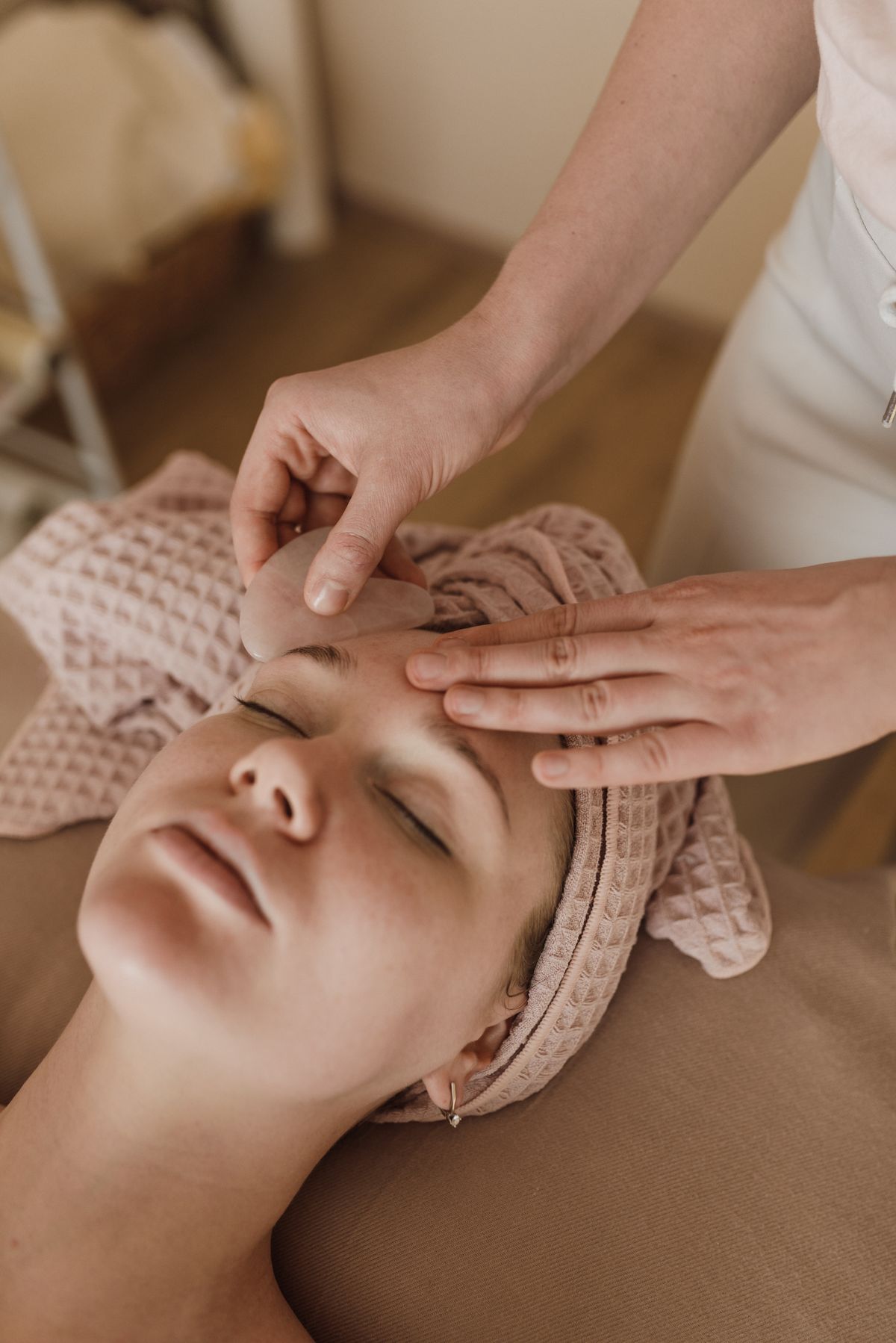 Therapist smoothing a pink gua sha stone across a relaxed client's forehead